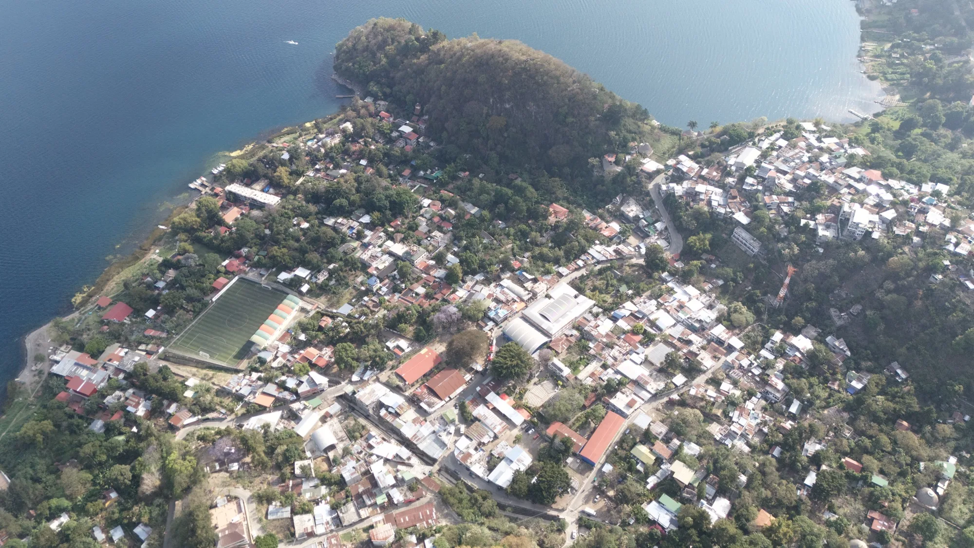 Aerial overhead view of San Marcos La Laguna, the village tightly bound by the lake on one side and the steep hillside behind it